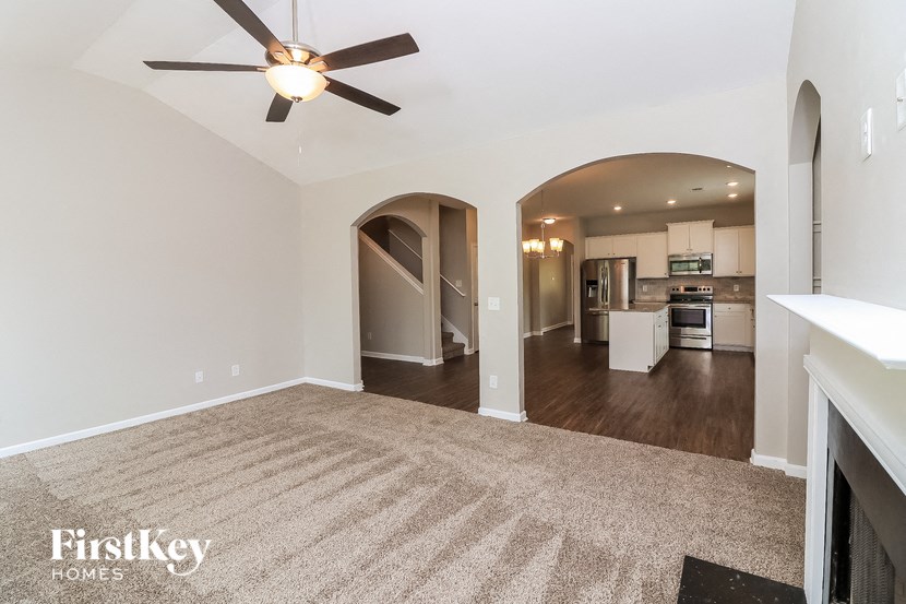 an empty living room with a ceiling fan and a kitchen