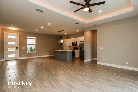 an empty living room with a kitchen and a ceiling fan