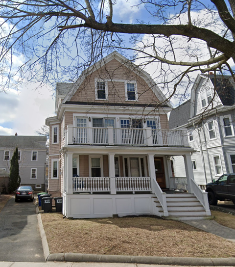 A two-story house with a white porch and a brown roof.
