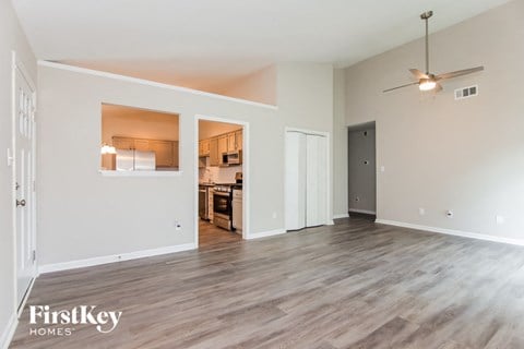 A spacious room with a kitchen visible through a window in the background.