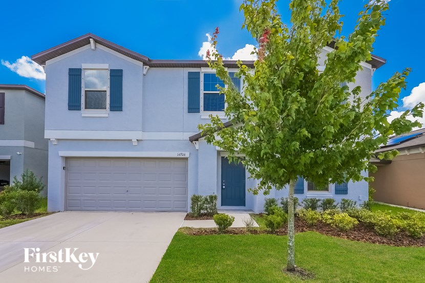 A white house with a grey garage door and a tree in front.