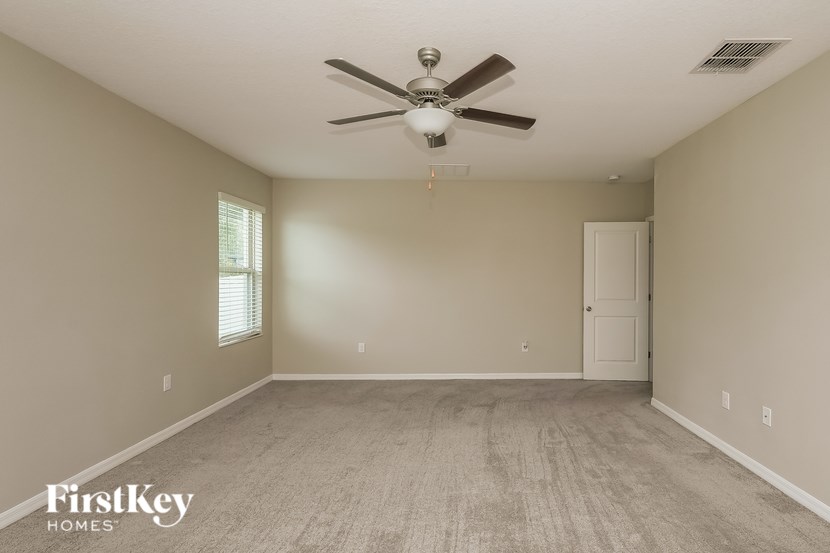 A spacious room with a ceiling fan and light fixture, carpeted floor, and a door on the right.