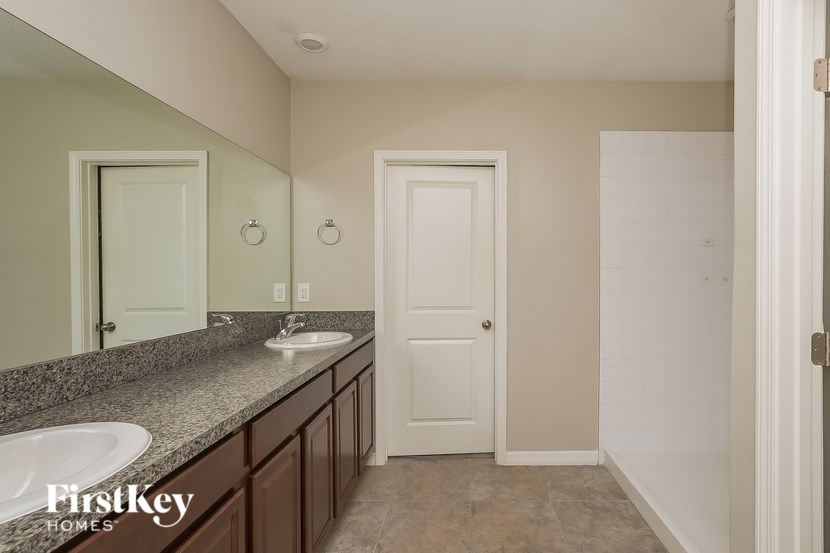 A bathroom with a sink and mirror in the foreground and a door in the background.