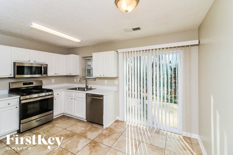 A kitchen with white cabinets and appliances, a tiled floor, and a sliding glass door.