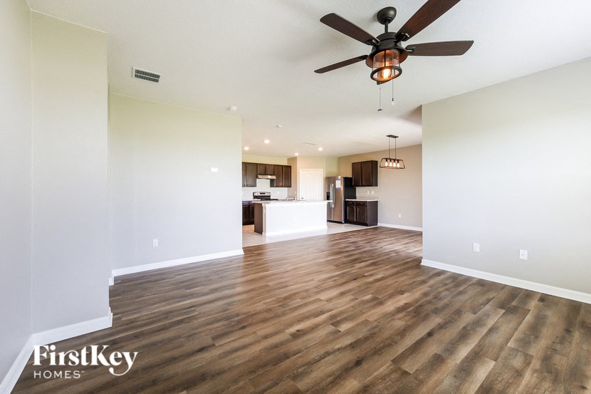 an empty living room with a ceiling fan and a kitchen