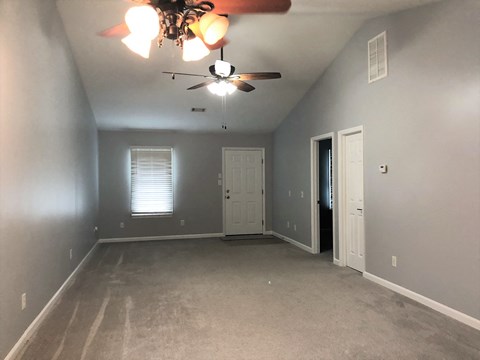 an empty living room with a ceiling fan and a door