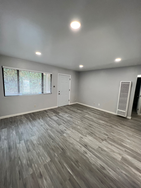 A room with a wooden floor and a window with blinds.