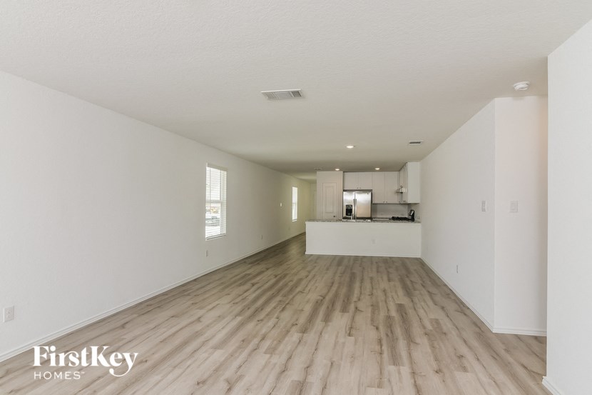 the living room and kitchen of an apartment with white walls and wood floors
