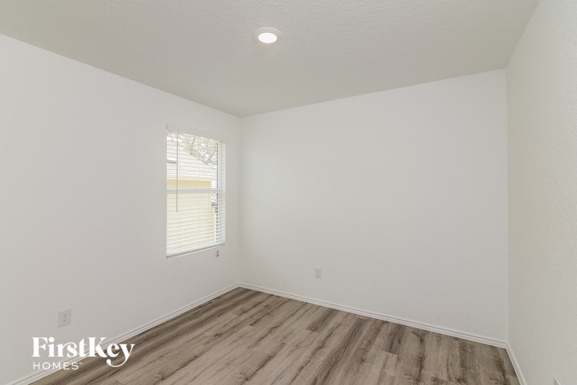 a bedroom with white walls and wood flooring and a window