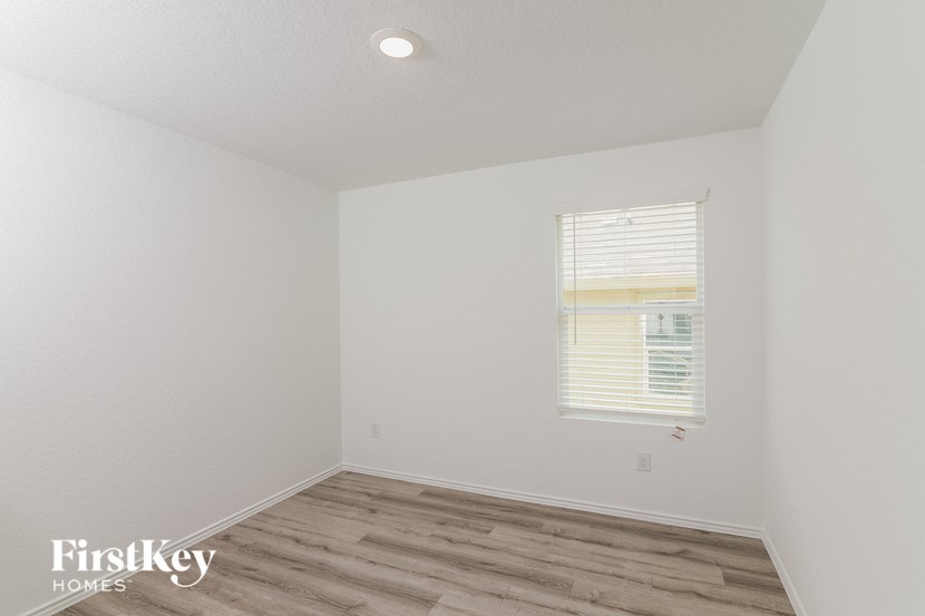 a bedroom with white walls and wood flooring and a window