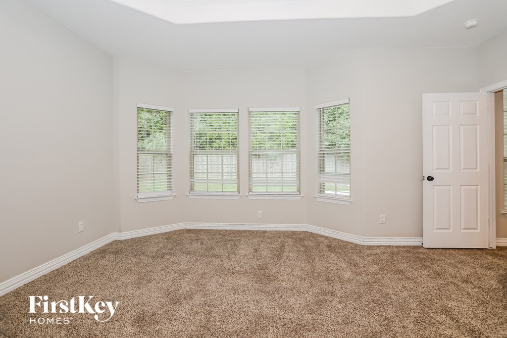 a bedroom with carpet and three windows and a white door