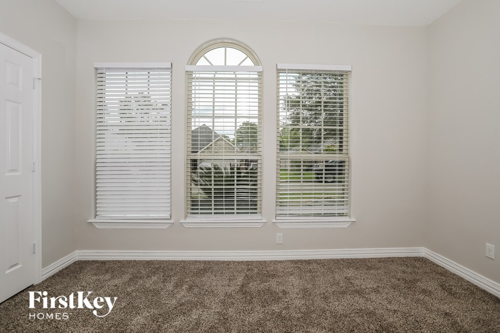 a living room with three windows and a carpeted floor