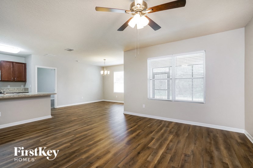 an empty living room with a ceiling fan and a kitchen