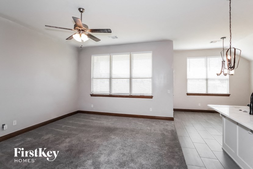 an empty living room with a ceiling fan and a kitchen