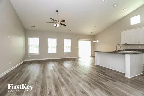 an empty living room with a kitchen and a ceiling fan