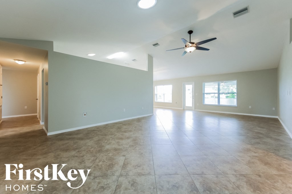 A spacious empty room with a ceiling fan and a light on.