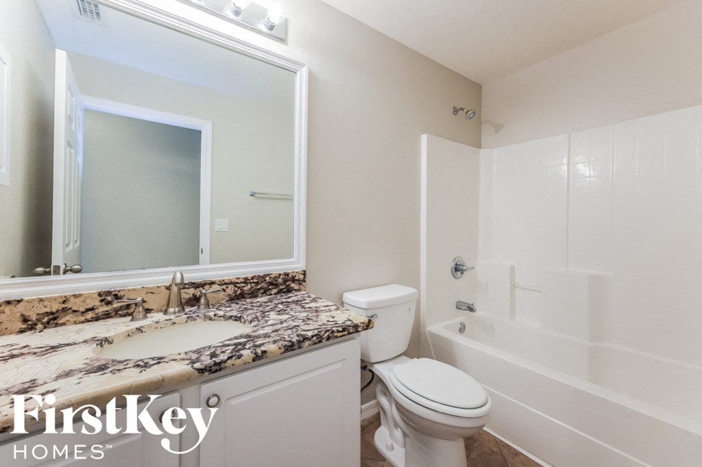 A bathroom with a marble countertop and white fixtures.