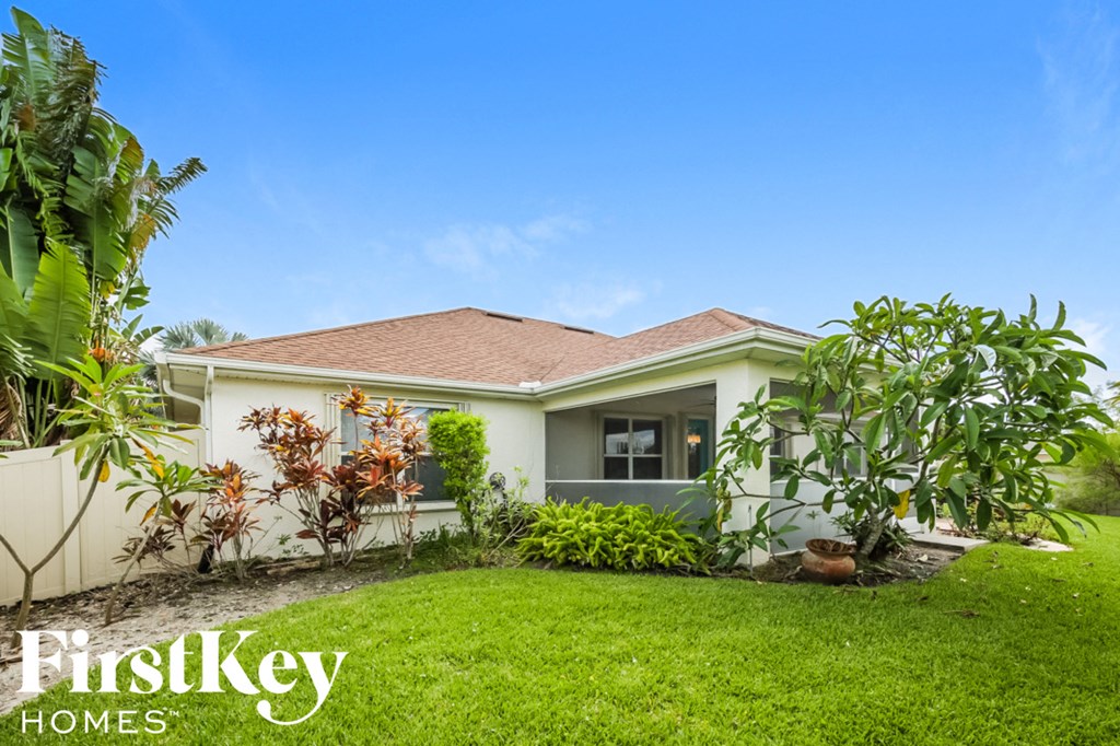 A house with a brown roof and a white fence is surrounded by greenery.