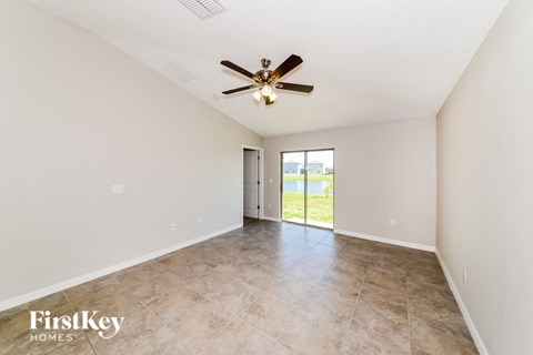 A spacious room with a ceiling fan and a sliding glass door leading to a balcony.