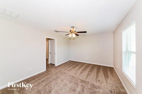 A carpeted room with a ceiling fan and a door.