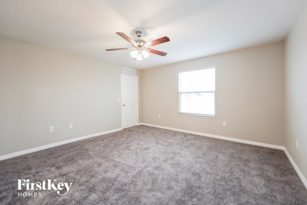 a carpeted room with a ceiling fan and a window