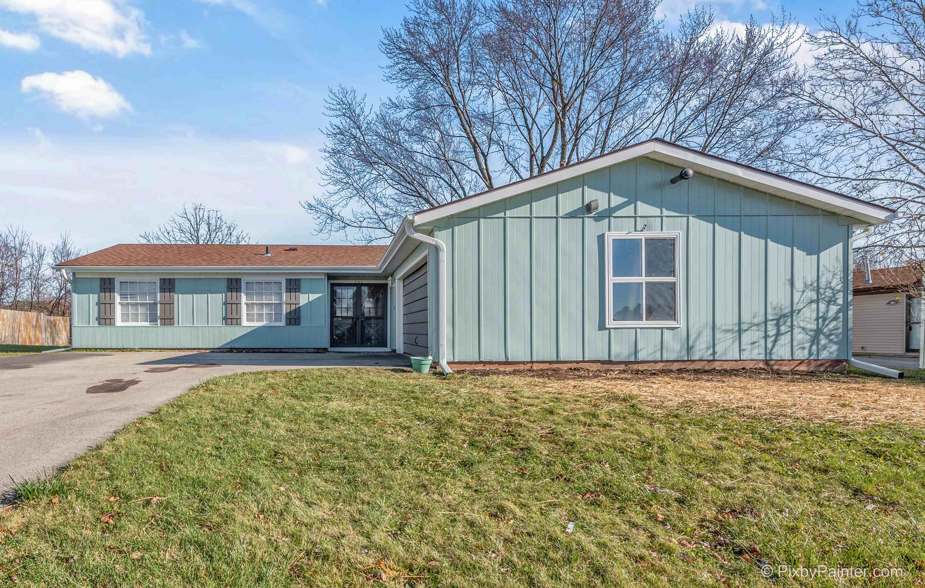 a green house with a driveway and a grassy yard