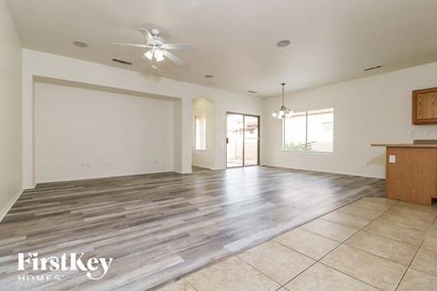 an empty living room with a kitchen and a ceiling fan