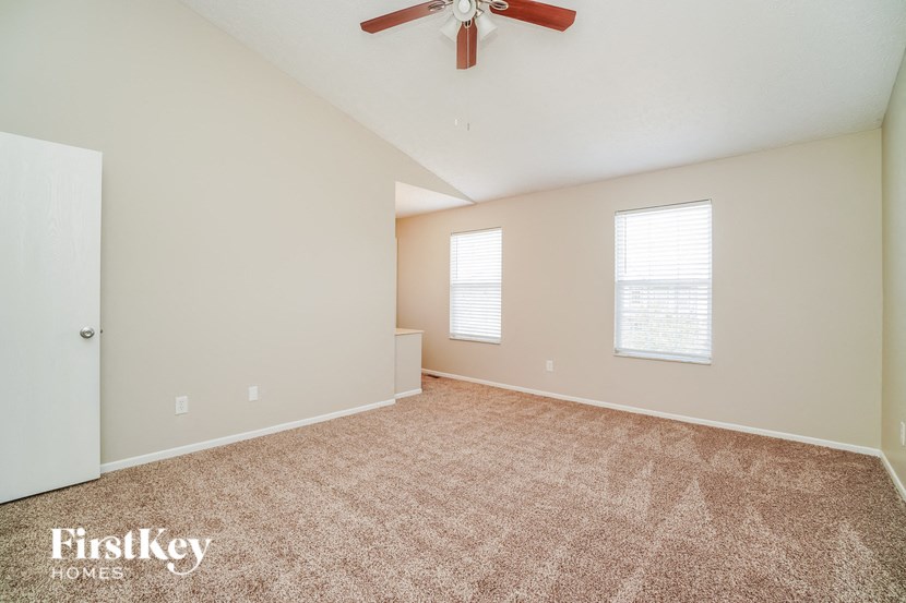 A room with a carpeted floor, a ceiling fan, and two windows.