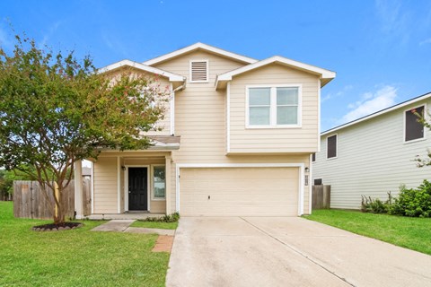 a beige house with a driveway and a tree
