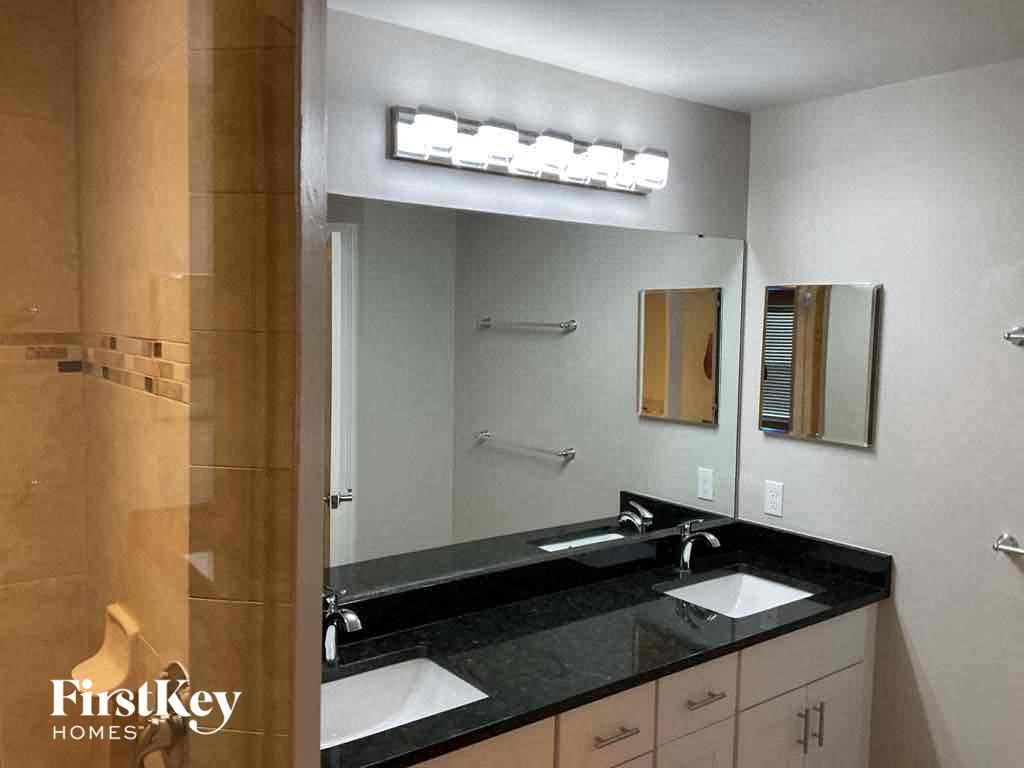 A bathroom with a black counter top and a mirror above it.