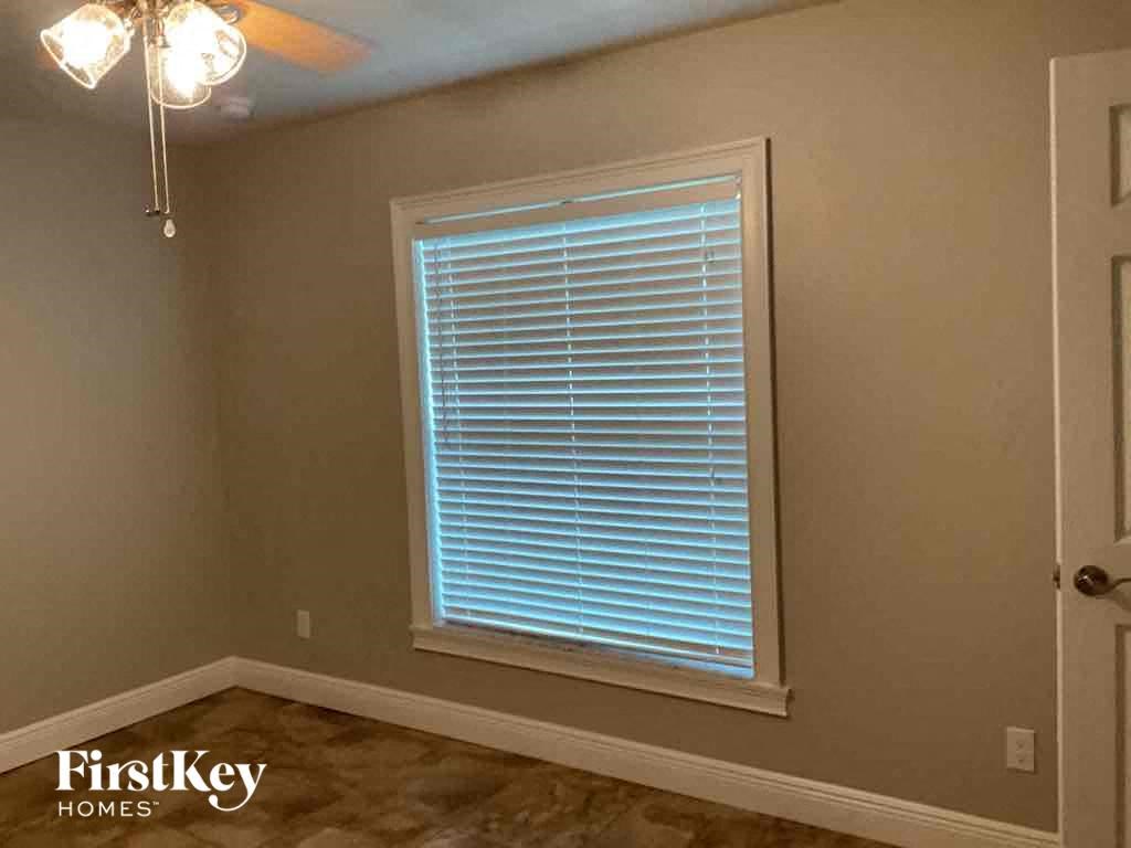 A room with a window covered in blinds and a chandelier hanging from the ceiling.