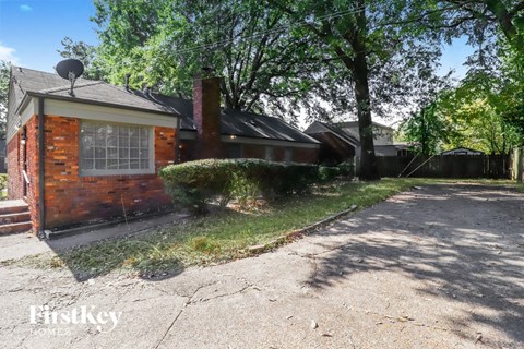 a small brick house with a driveway and trees