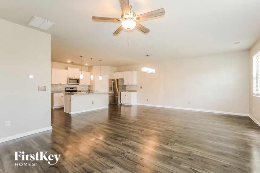 an empty living room with a ceiling fan and a kitchen