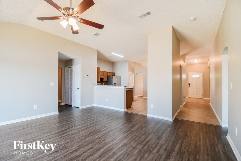 an empty living room with a ceiling fan and a kitchen