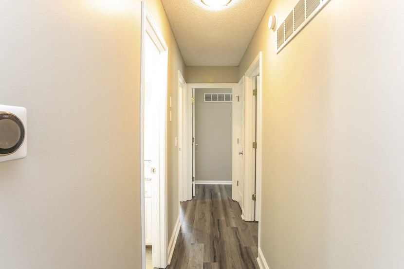 an empty hallway with wood flooring and white walls and a door to a bathroom