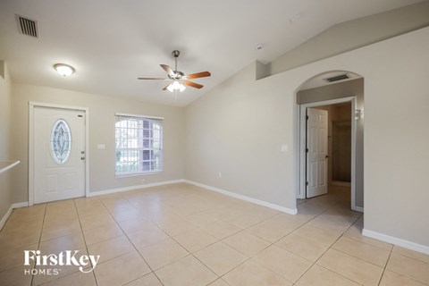 an empty living room with a ceiling fan and a door to a hallway