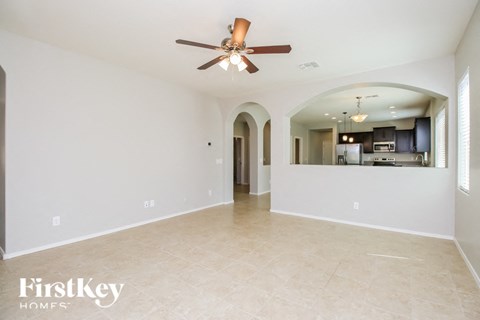 an empty living room with a ceiling fan and a kitchen