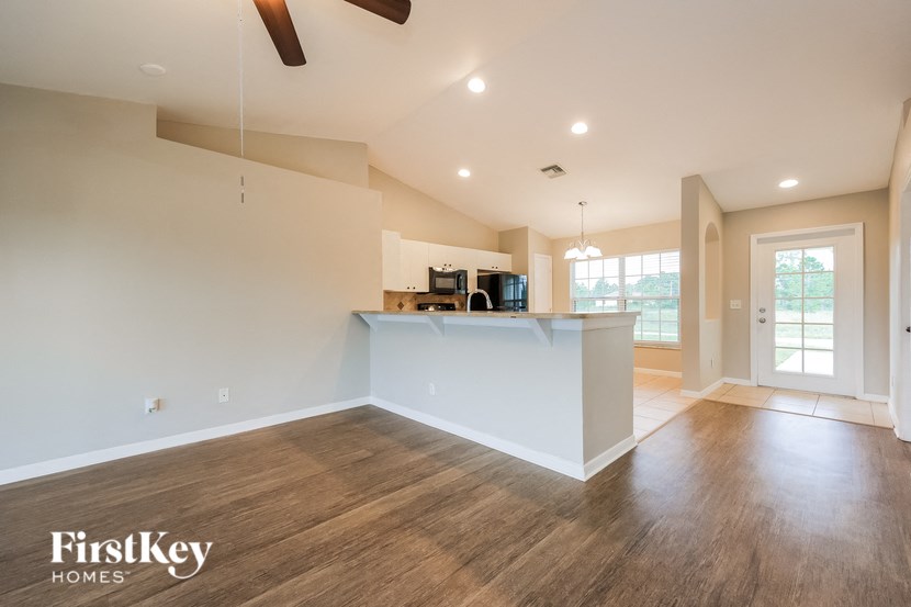 an empty living room with a kitchen and a ceiling fan