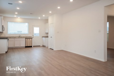 A spacious kitchen and living room with white walls and wooden floors.
