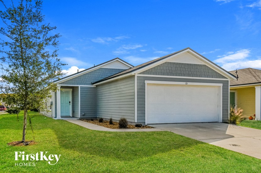 A house with a garage door and a tree in front of it.