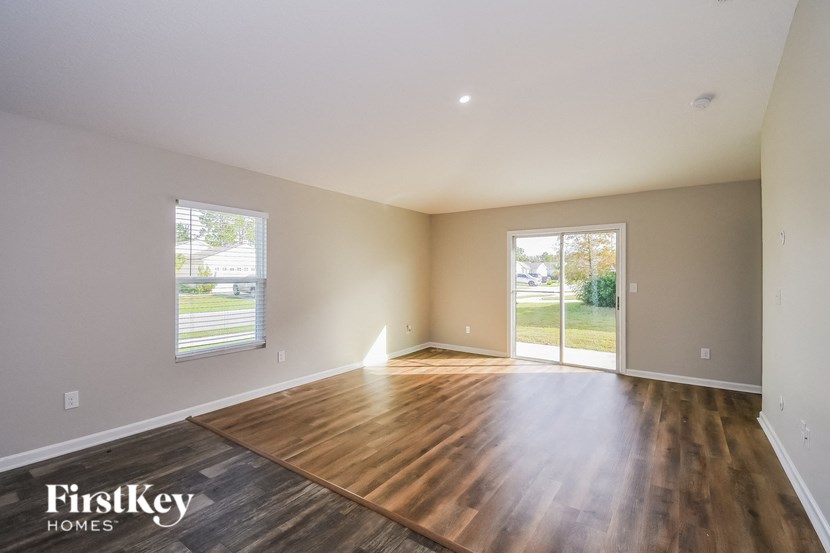 A spacious room with wooden flooring and a sliding glass door leading to a backyard.