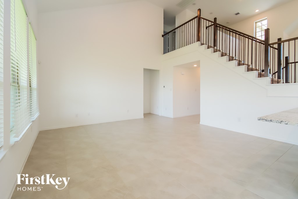 A spacious room with a staircase and a window with blinds.