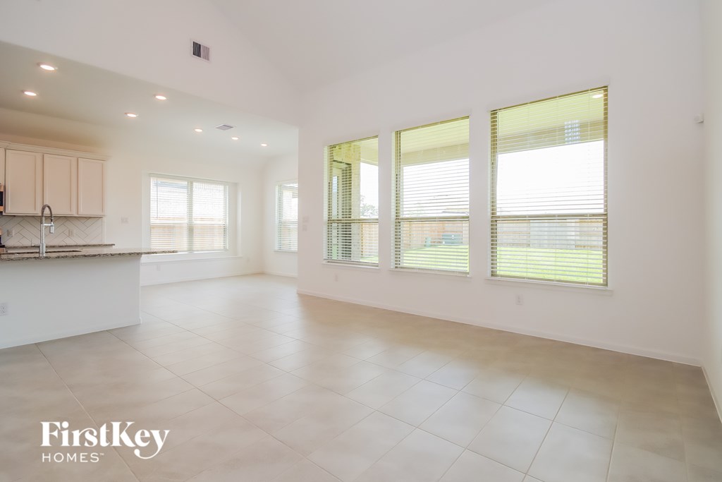 A spacious, empty room with a kitchen area to the left and a window with blinds on the right.