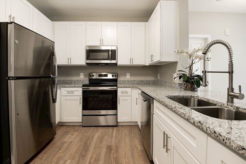 A kitchen with a black refrigerator, white cabinets, and a granite countertop.