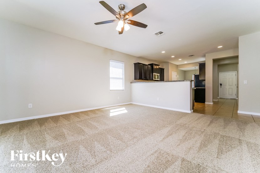 an empty living room with a ceiling fan and a kitchen