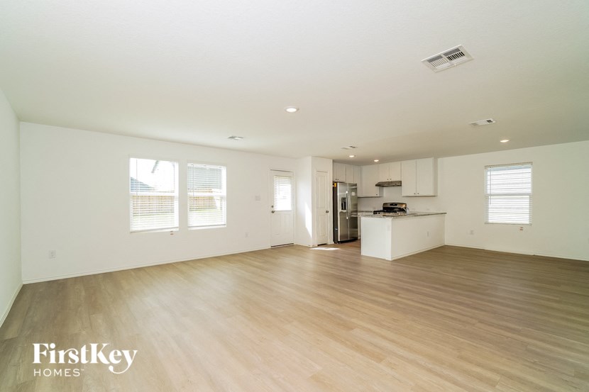 A spacious empty room with wooden flooring and a kitchen area in the background.
