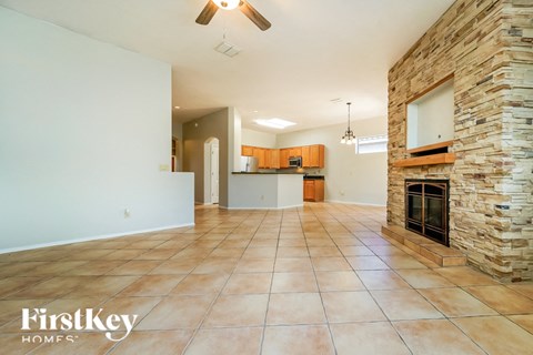 A spacious living room with a stone fireplace and a kitchen in the background.