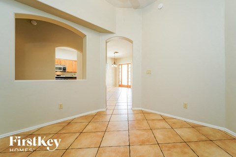 A hallway with a tile floor and a view of a kitchen through an arched doorway.