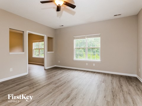 A spacious room with a ceiling fan and light, wooden flooring, and two windows.