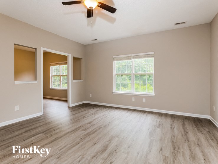 A spacious room with a ceiling fan and light, wooden flooring, and two windows.